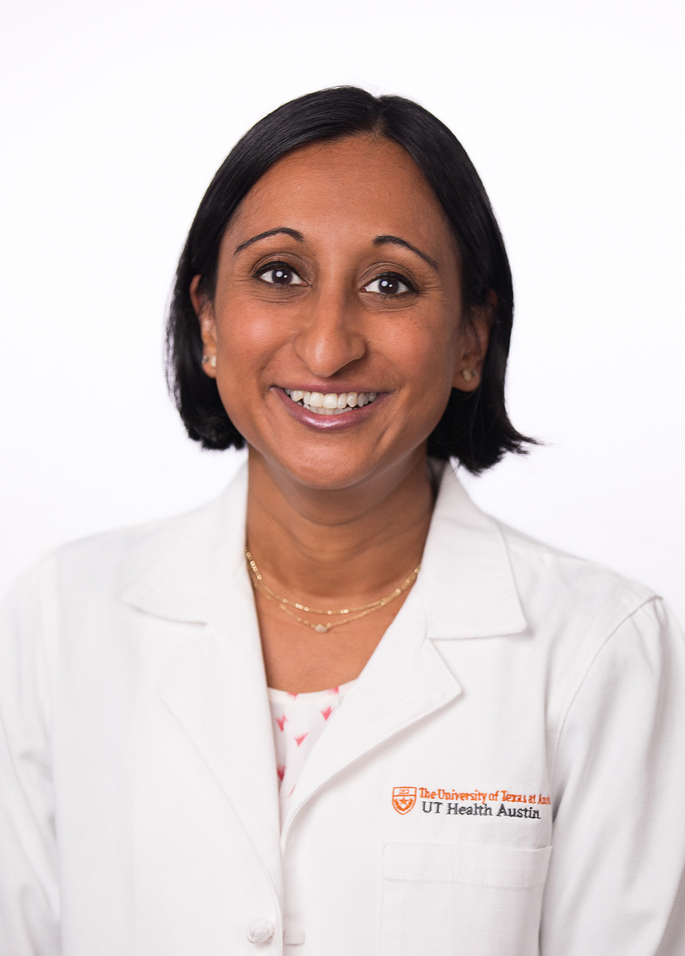 Dr. Saradha Subramanian wearing a white coat and smiling in front of a white backdrop.