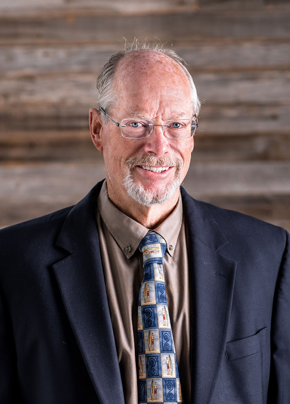 Pediatric cardiologist Stuart Rowe, MD, smiling in front of a wooden wall. He is wearing a navy suit and patterned tie.