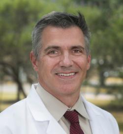 Dr. Zachary Chipman wearing a white coat and smiling outdoors.