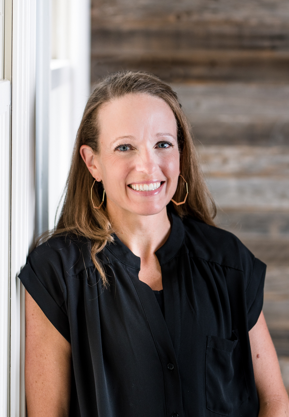 Julie Manning wearing a black blouse and smiling in front of a wooden wall.