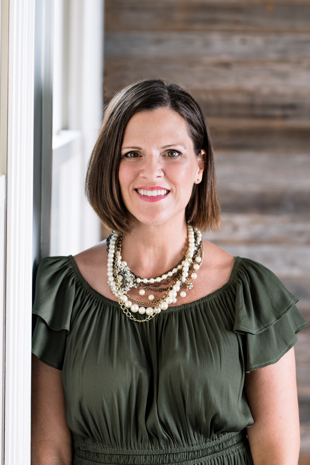 Kristy Neff wearing a green blouse and smiling in front of a wooden wall.