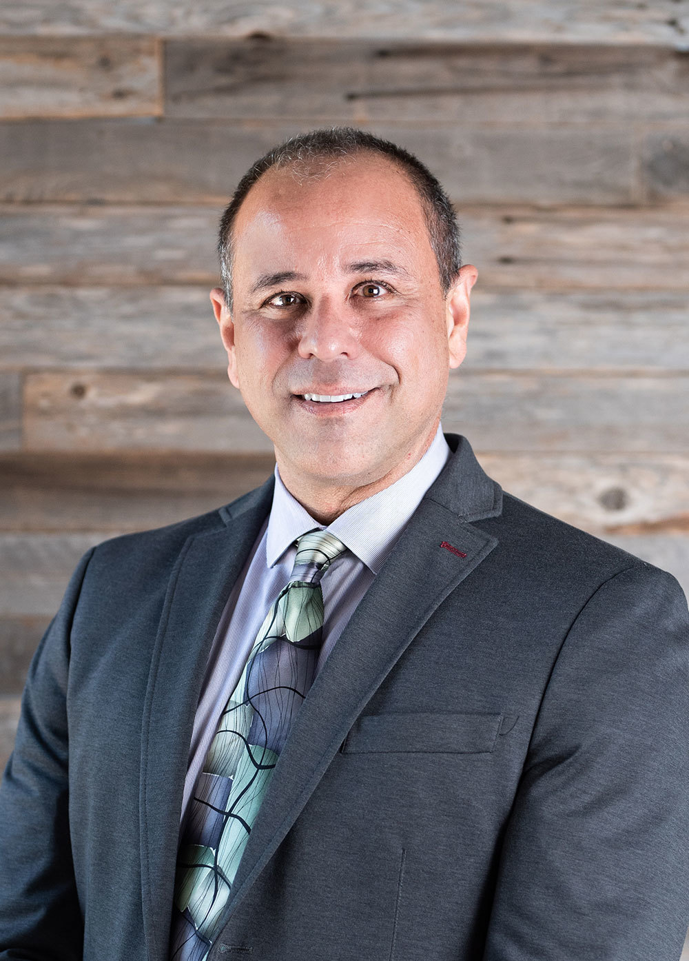 Pediatric cardiologist Kenneth Shaffer, MD, wearing a suit and tie and smiling in front of a wooden wall.