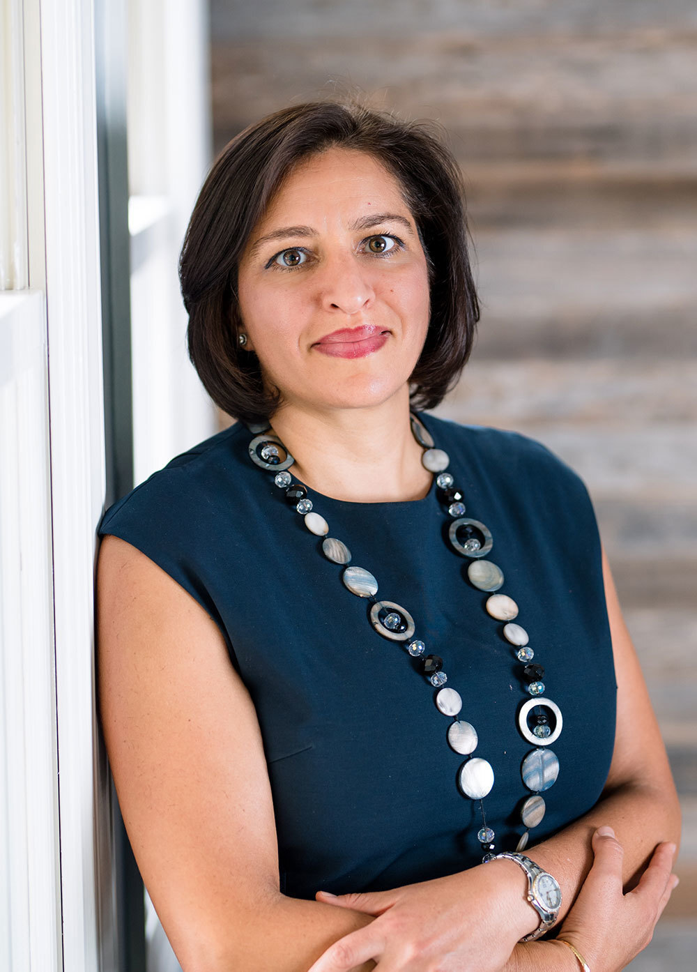 Dr. Keren Hasbani wearing a dark blouse and smiling in front of a wooden wall.