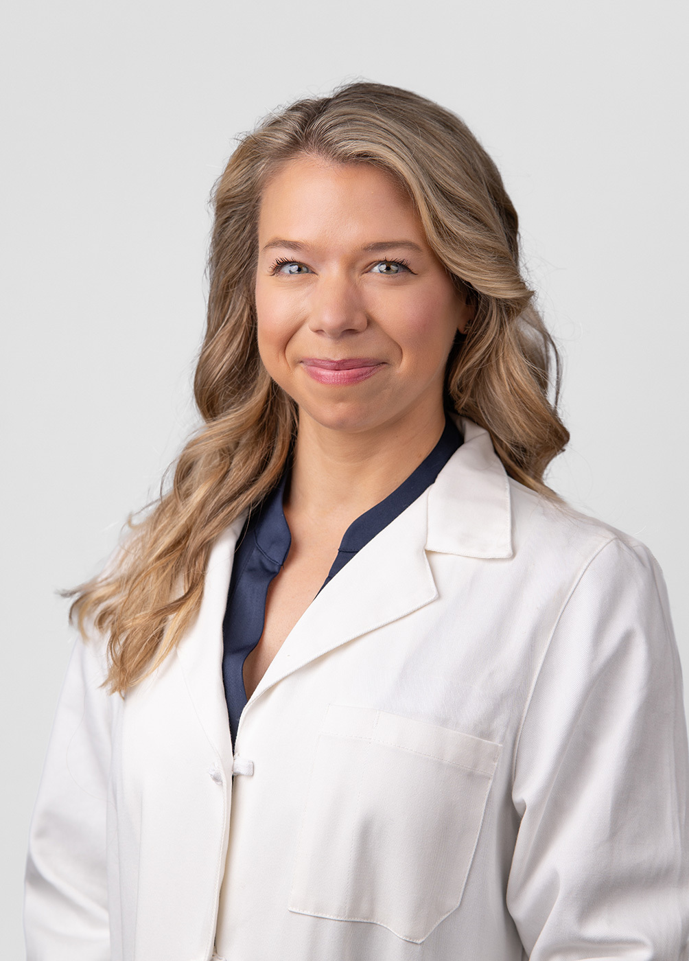 A headshot of Maggie Goss. She is wearing a black blouse and a white coat.
