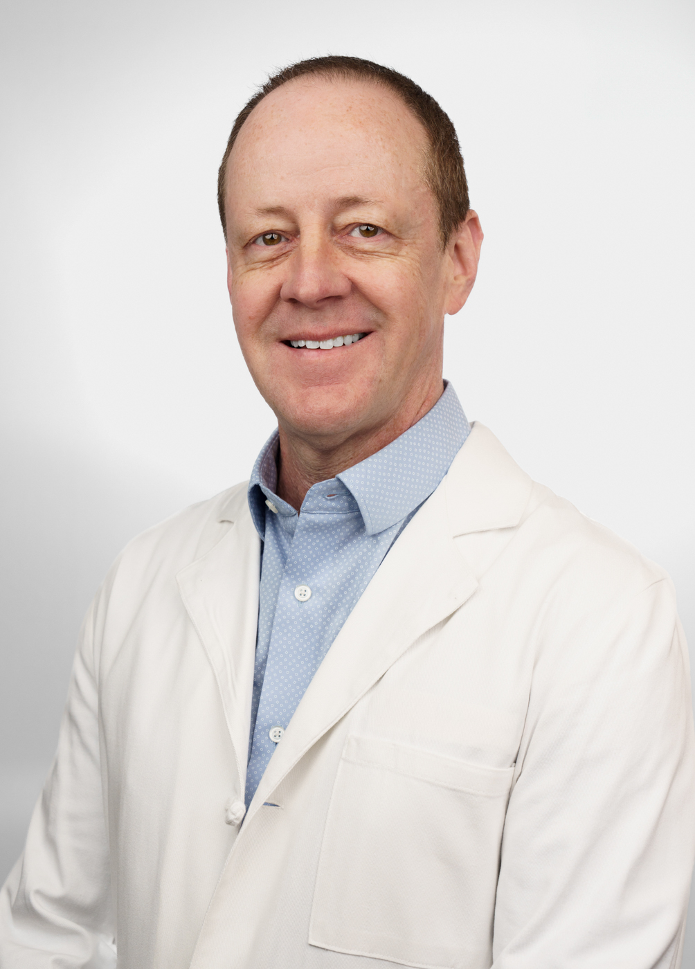 Headshot of Richard O'Brien. He is wearing a blue dress shirt and a white coat.