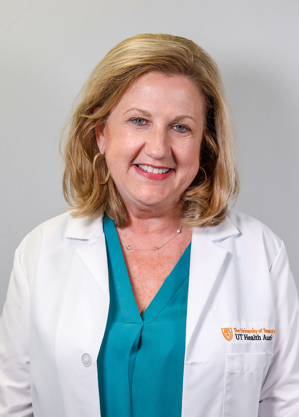 Sally Monahan wearing a white coat and smiling in front of a white backdrop.